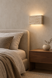 Lumo travertine wall light beside a neutral upholstered bed